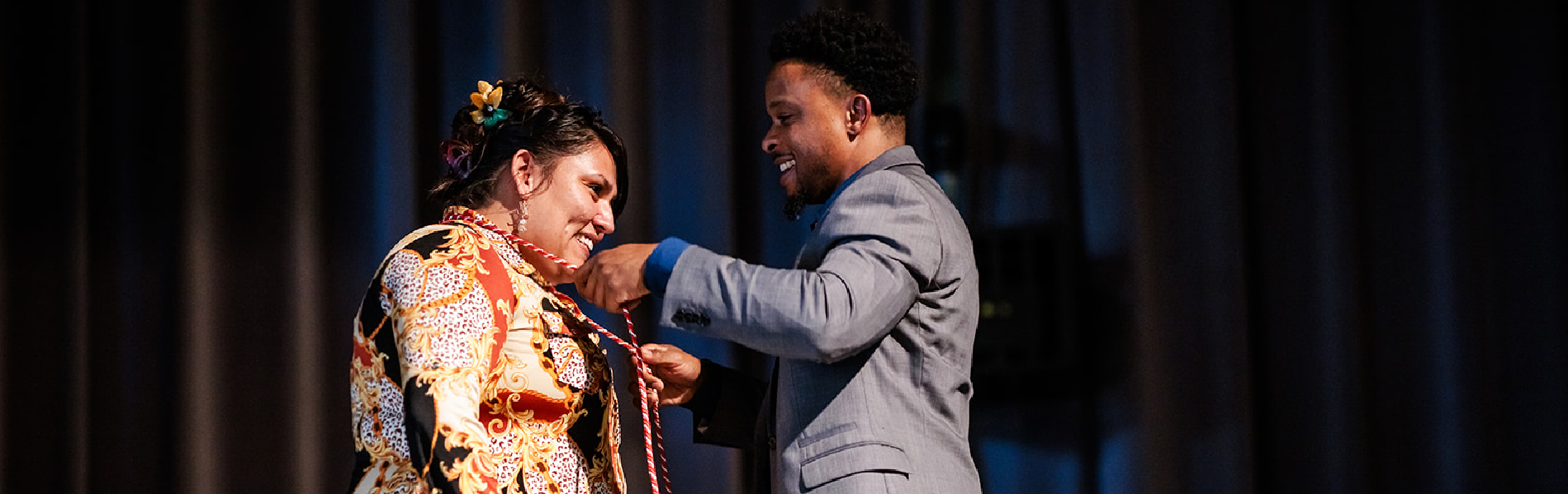 man placing honor cord on smiling graduate